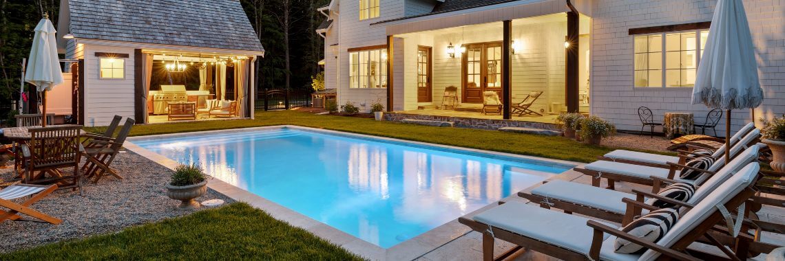 Nighttime view of lit landscaped back yard with pool and pool house